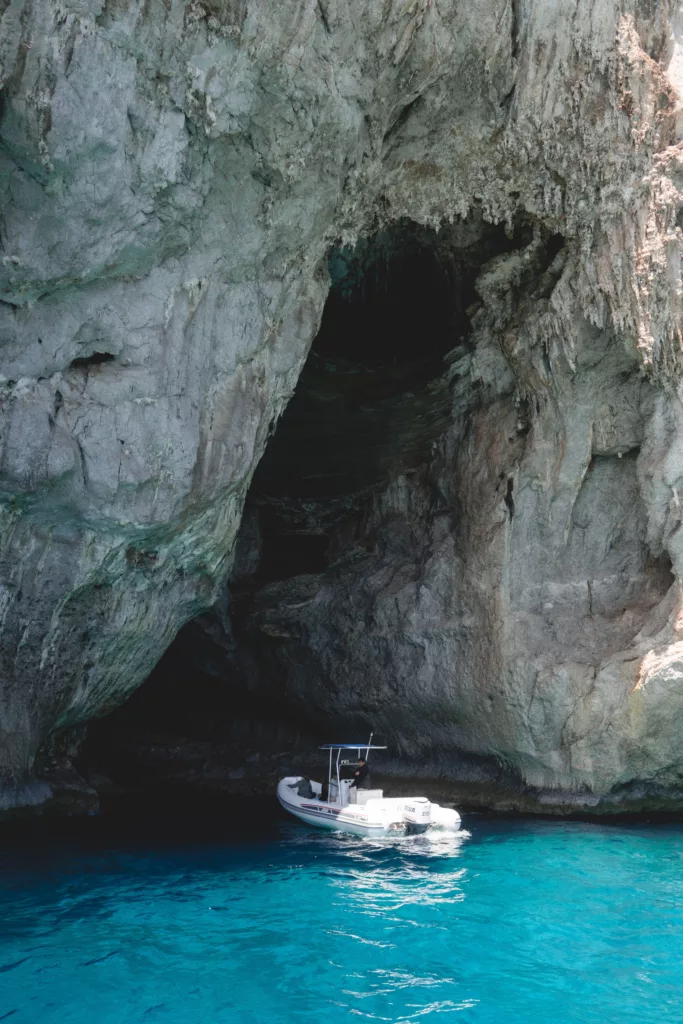 A scenic view outside the Blue Grotto, featuring crystal-clear turquoise waters surrounded by rugged cliffs.