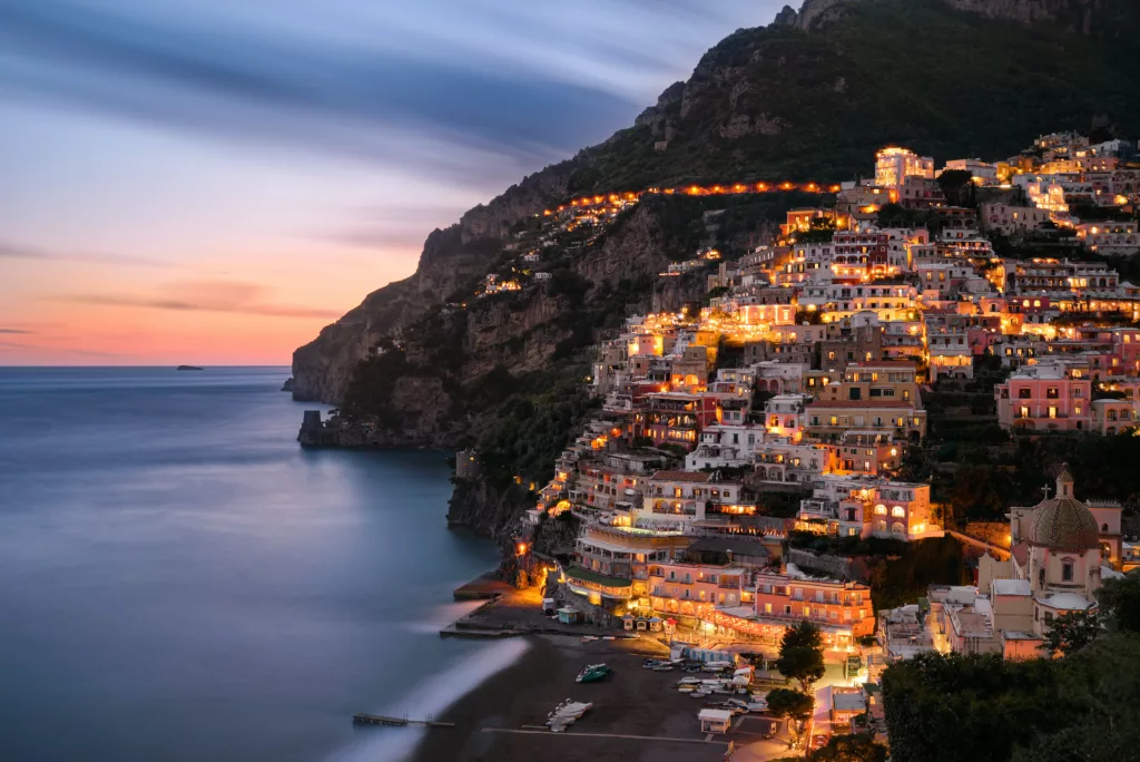 A breathtaking seaside sunset in Positano, Campania, with vibrant hues of orange and pink reflecting on the calm waters of the Mediterranean.